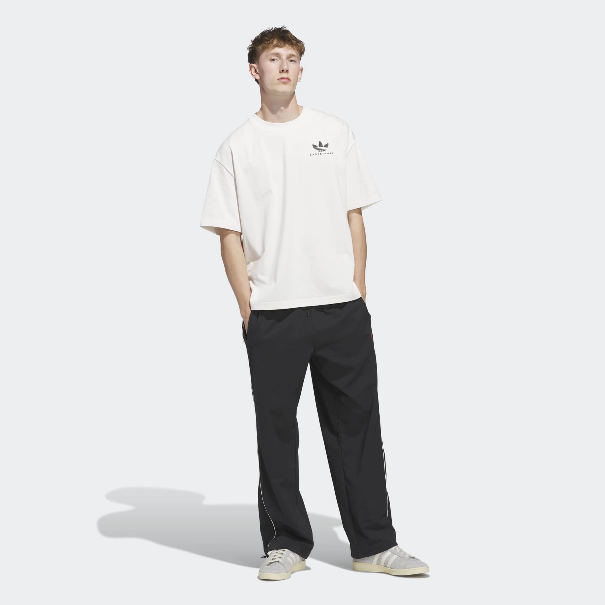 „Frontansicht Model des Adidas Originals Worldwide Hoops GFX Tee in Cloud White – Weißes Baumwoll-T-Shirt mit schwarzem Basketball-Grafikprint bei Stickabush Berlin.“