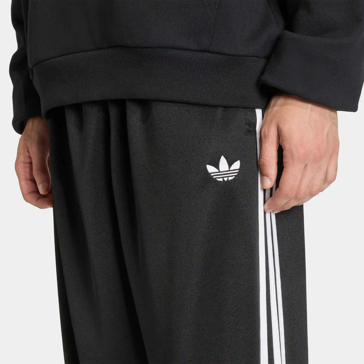 adidas Originals Adicolor Loose Tracksuit Pants in Black – Vorderansicht am Model der schwarzen Trainingshose mit den ikonischen 3-Stripes und lockerem Schnitt.