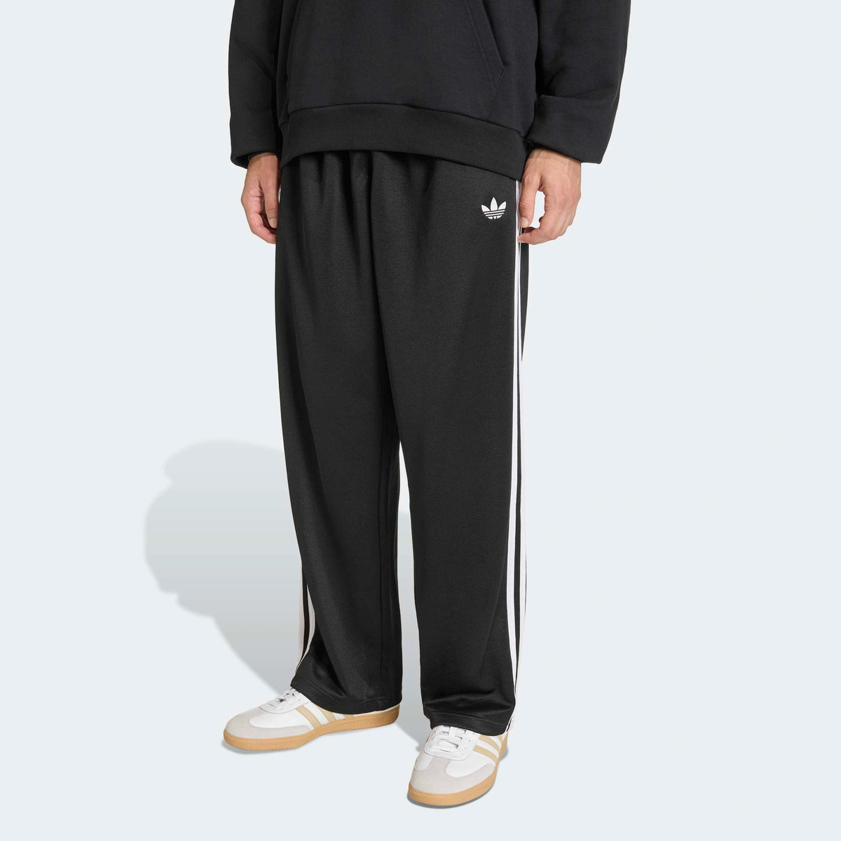adidas Originals Adicolor Loose Tracksuit Pants in Black – Vorderansicht am Model der schwarzen Trainingshose mit den ikonischen 3-Stripes und lockerem Schnitt.