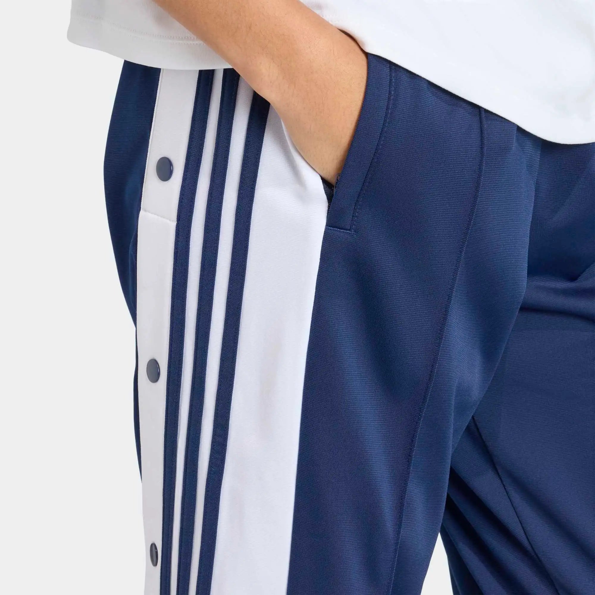 „Dunkelblaue Adidas Originals Adibreak Trainingshose für Damen (Night Indigo) mit durchgehenden Druckknöpfen und weißen Streifen bei Stickabush Berlin.“