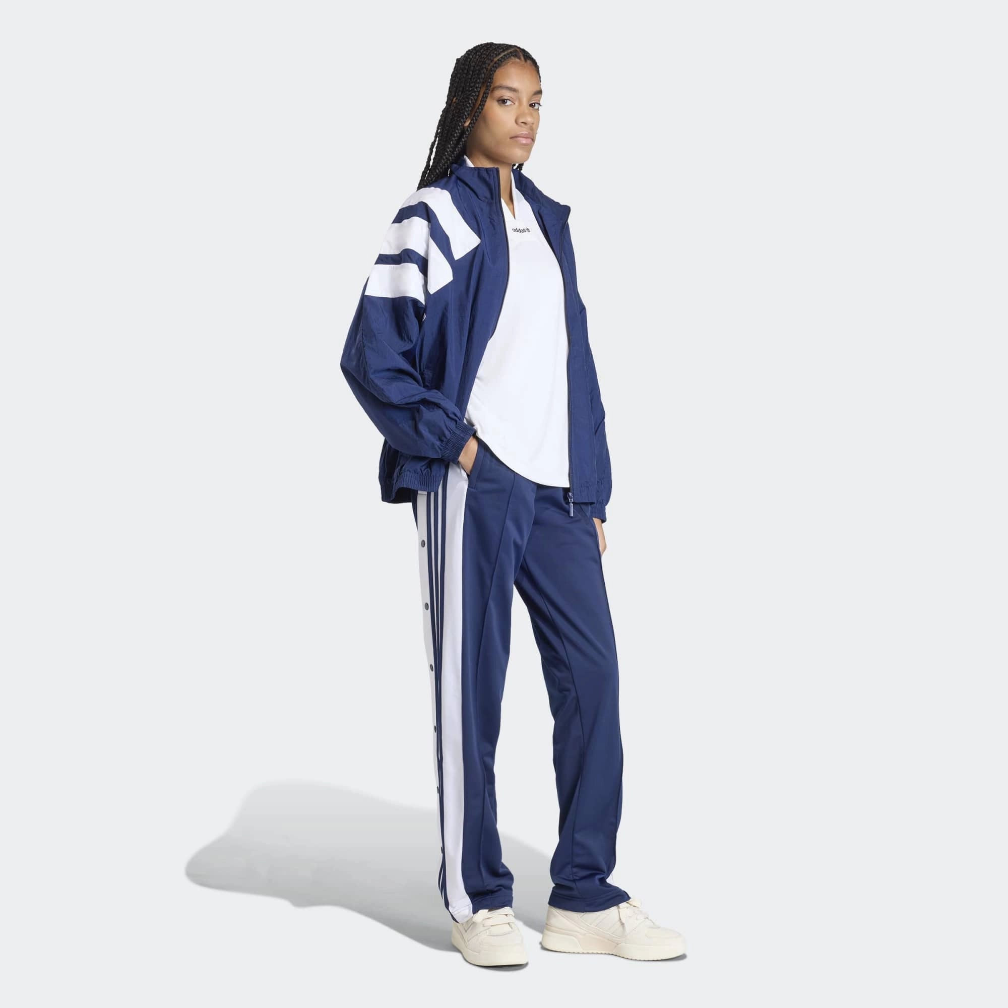 „Dunkelblaue Adidas Originals Adibreak Trainingshose für Damen (Night Indigo) mit durchgehenden Druckknöpfen und weißen Streifen bei Stickabush Berlin.“