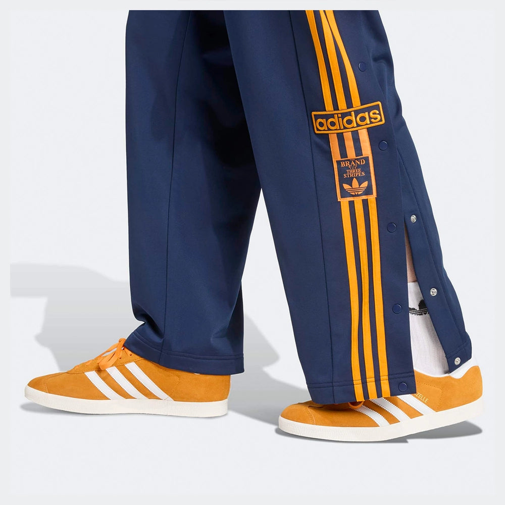 "Adidas Adibreak Track Pants in Blau/Orange, 100% recyceltes Trikot-Material, mit orangefarbenen 3-Streifen und seitlichen Druckknöpfen.“