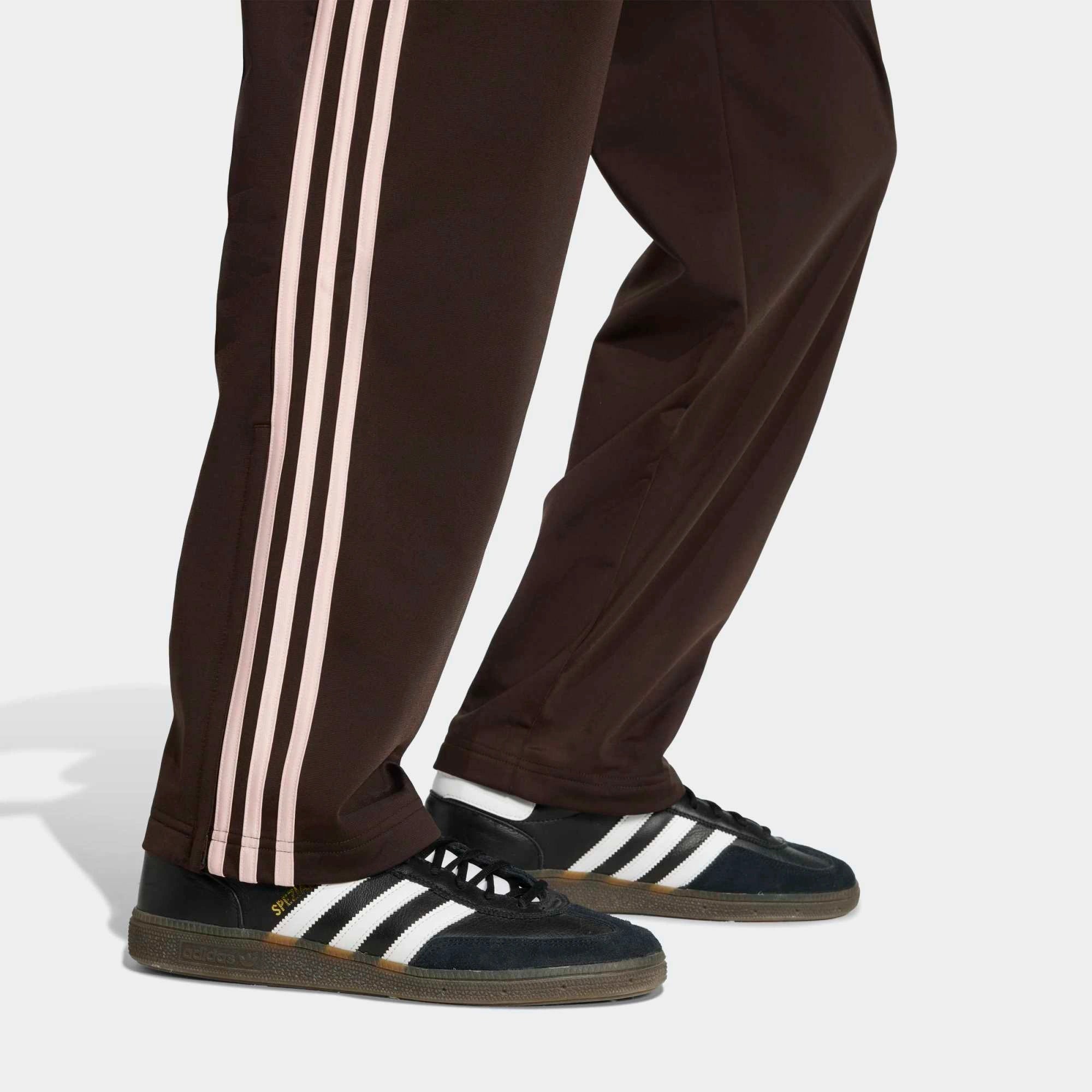 “Seitenansicht Hosenbein Detail der Adidas Originals Firebird Track Pants in Aurora Coffee (Braun) mit weißen Streifen – Klassische Retro-Hose bei Stickabush Berlin.“