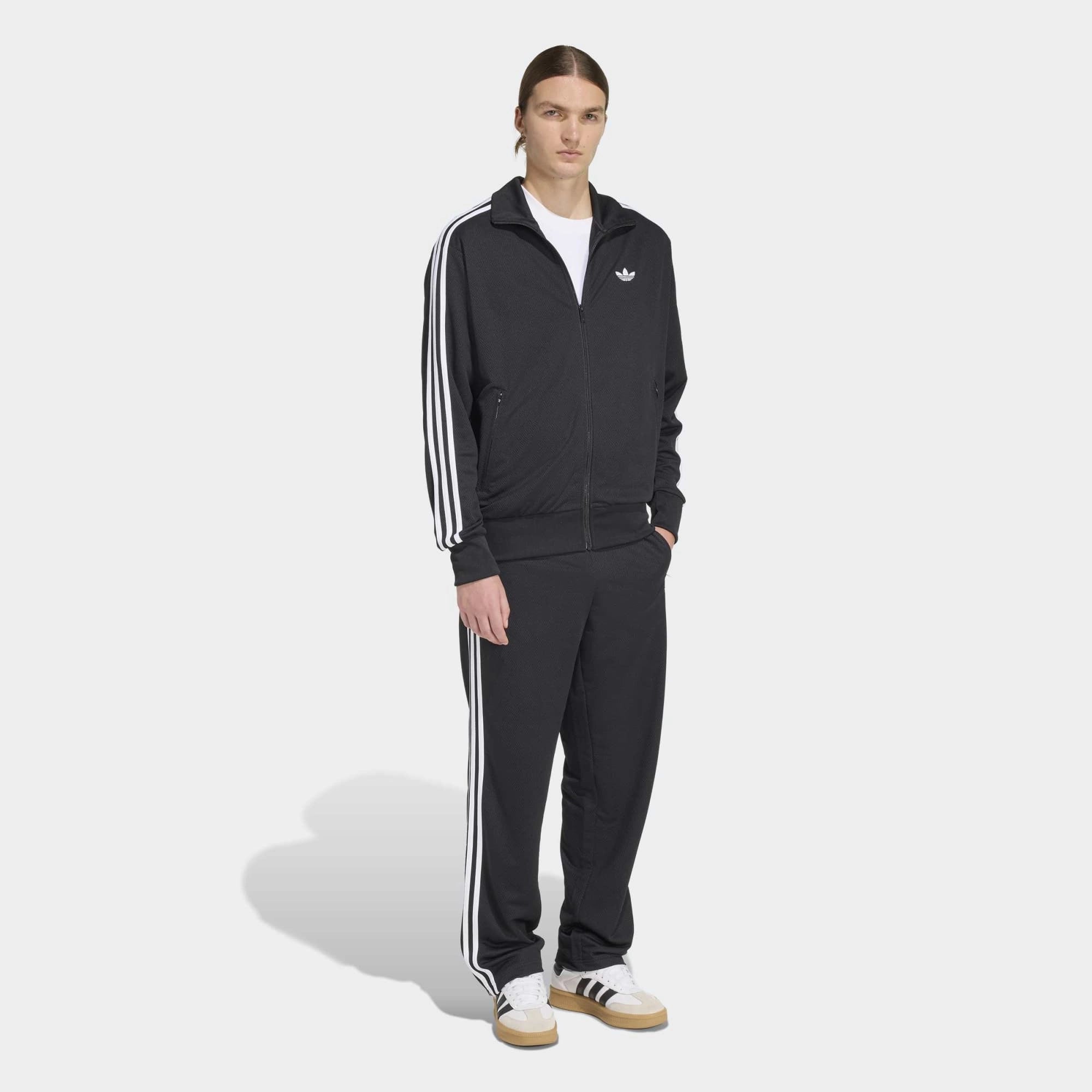 “Adidas Originals Firebird Track Pants Mesh in Schwarz mit weißen Streifen, Frontansicht des Trefoil-Logos und Mesh-Textur bei Stickabush Berlin.“
