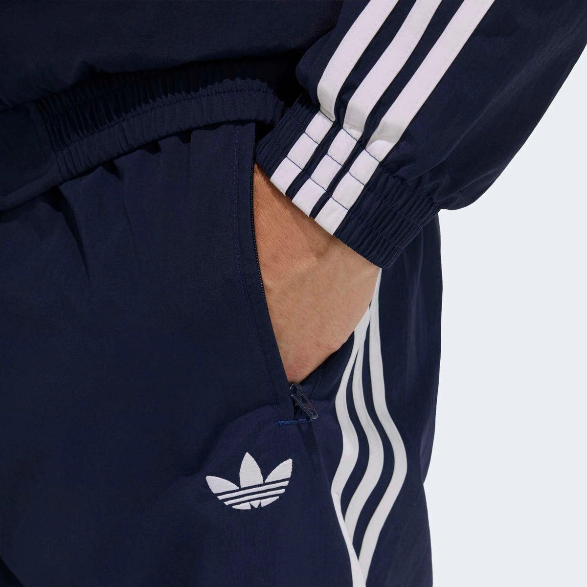 “Die adidas Originals Firebird Woven Trainingshose in Night Indigo (Dunkelblau) mit weißen 3-Streifen und leichtes, strapazierfähiges Webmaterial (Woven) bei Stickabush“.