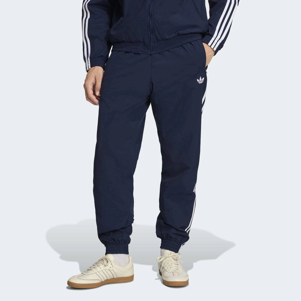 “Die adidas Originals Firebird Woven Trainingshose in Night Indigo (Dunkelblau) mit weißen 3-Streifen und leichtes, strapazierfähiges Webmaterial (Woven) bei Stickabush“.