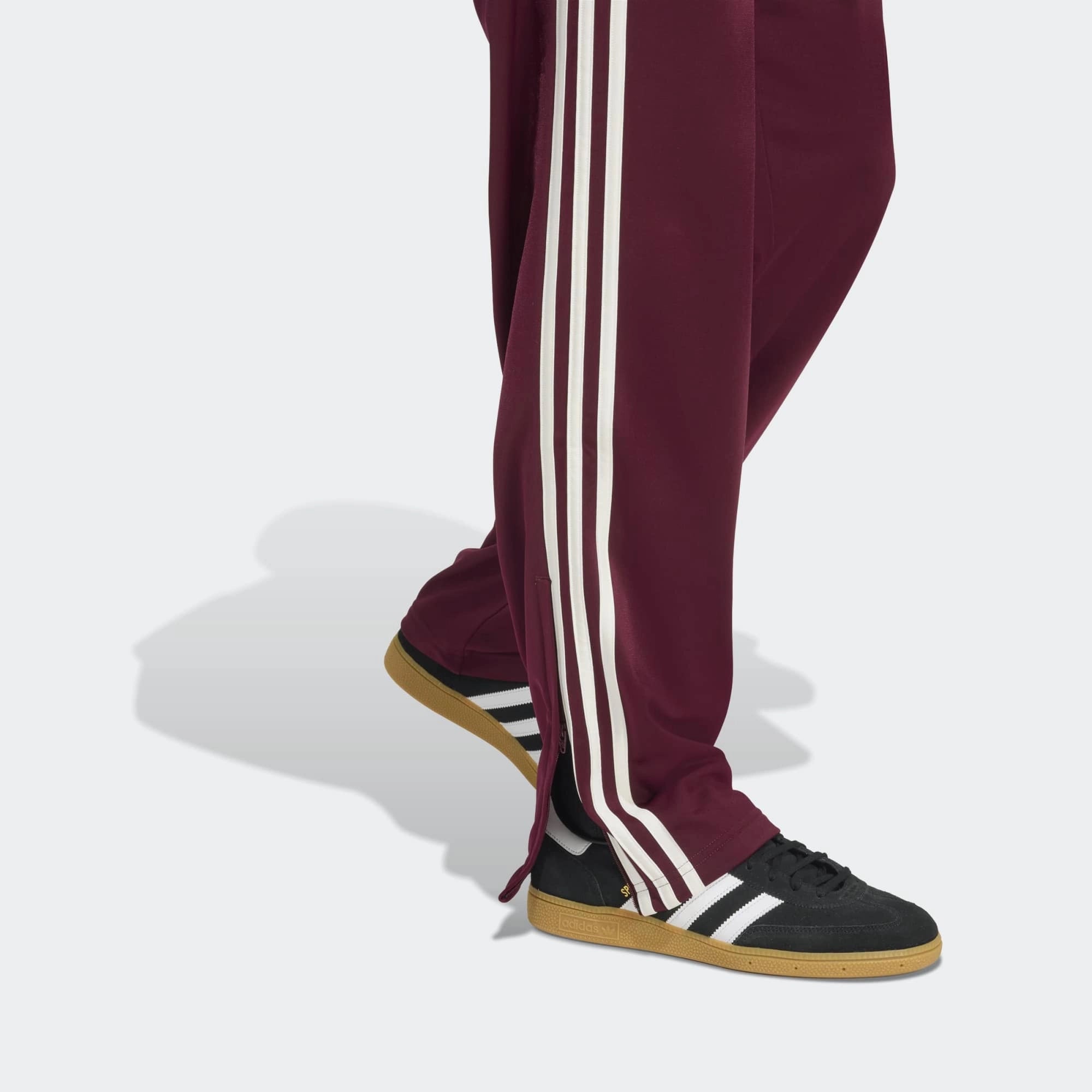 „Frontansicht Detail der Adidas Originals Firebird Track Pants in Maroon (Dunkelrot) mit cremeweißen 3-Streifen – Klassische Retro-Trainingshose bei Stickabush Berlin.“