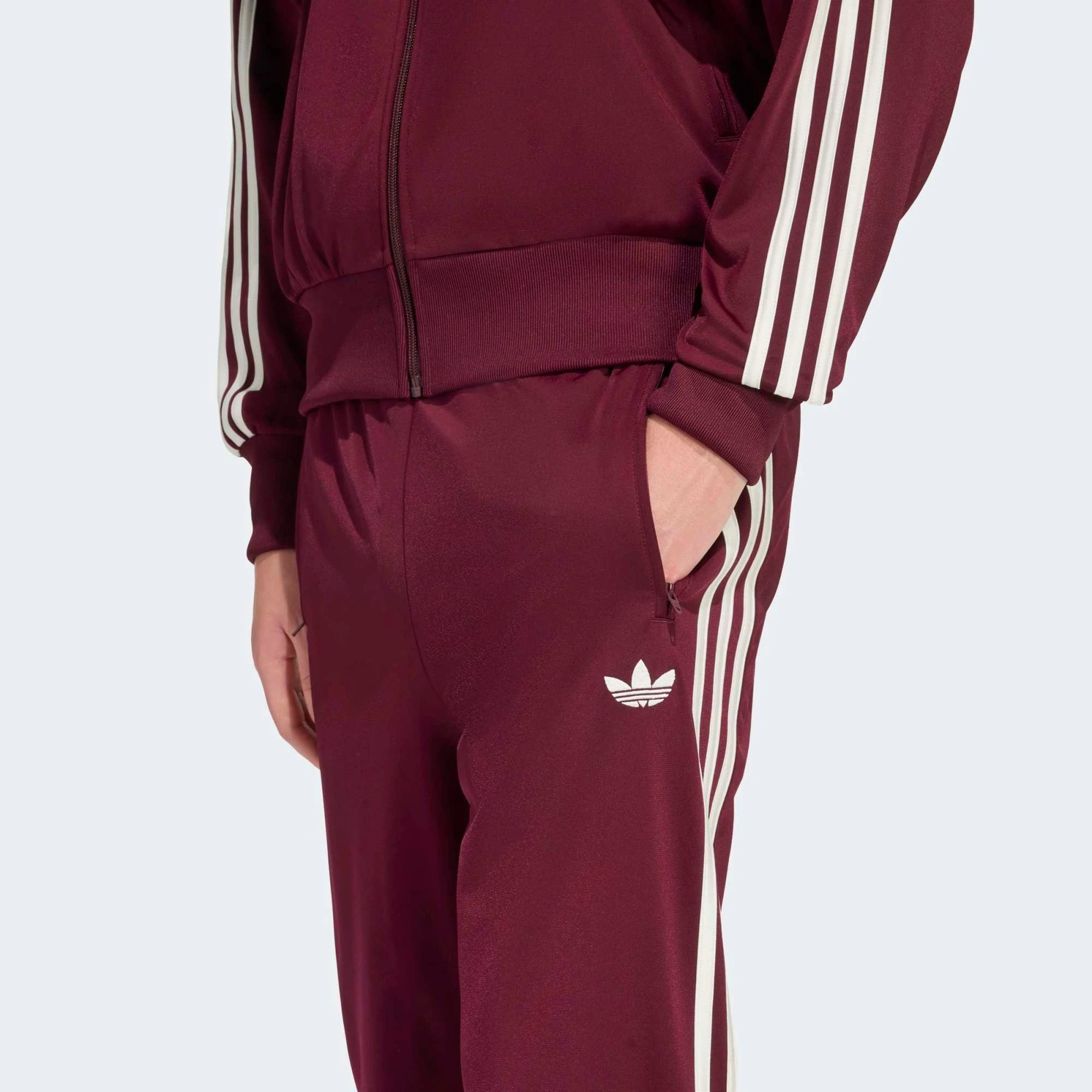 „Frontansicht Detail Model der Adidas Originals Firebird Track Pants in Maroon (Dunkelrot) mit cremeweißen 3-Streifen – Klassische Retro-Trainingshose bei Stickabush Berlin.“