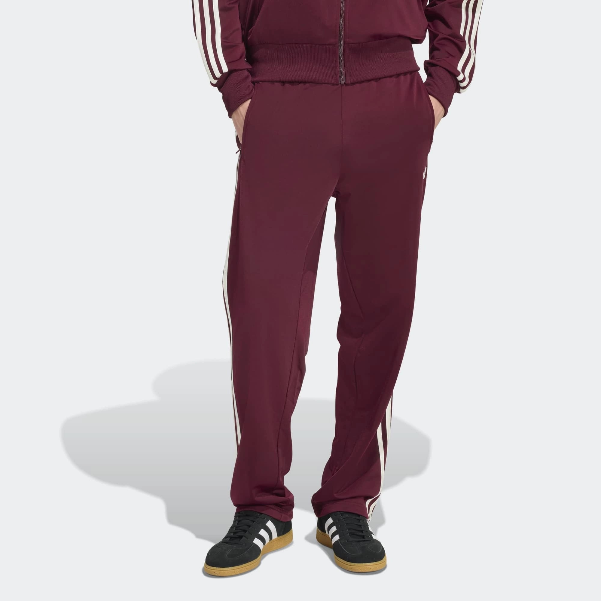 „Vorderansicht Outfit Model der Adidas Originals Firebird Track Pants in Maroon (Dunkelrot) mit cremeweißen 3-Streifen – Klassische Retro-Trainingshose bei Stickabush Berlin.“