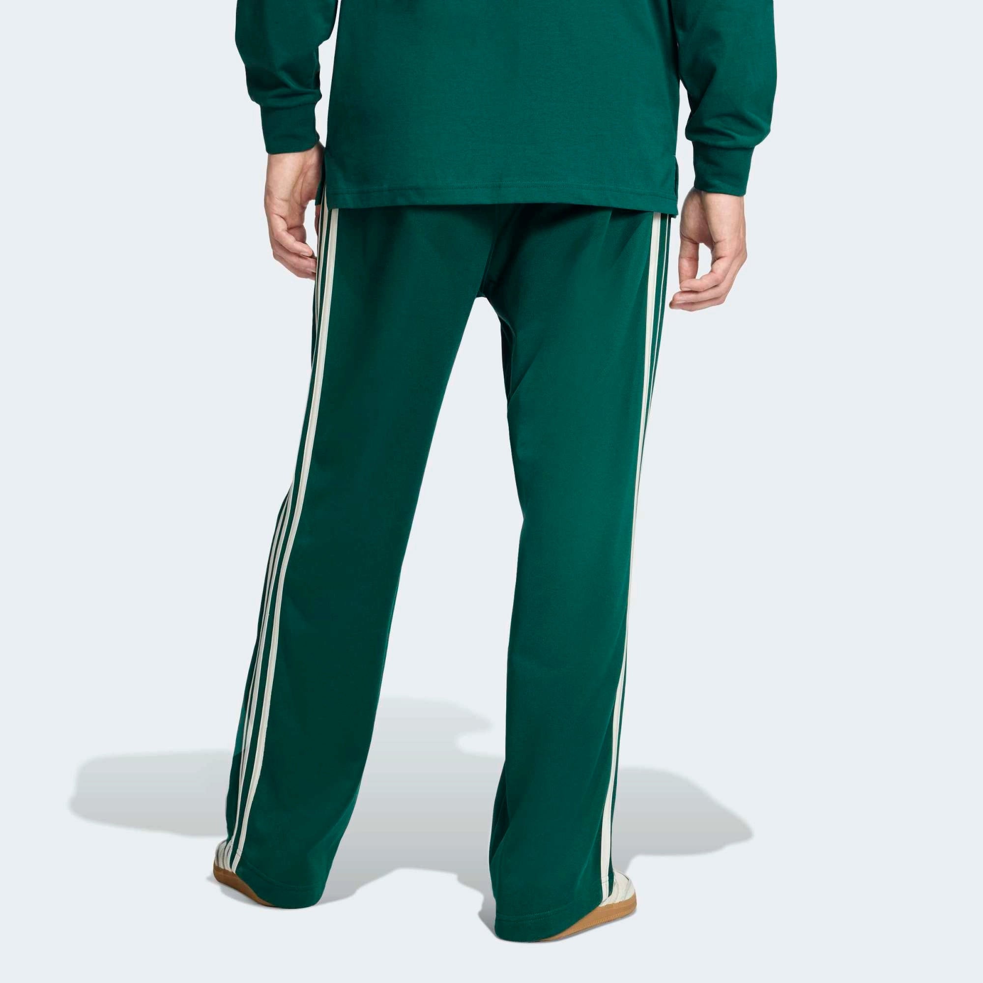 “Hinteransicht Model der adidas Originals Baggy Track Pants in Collegiate Green mit weißen 3-Streifen, seitlichen Reißverschlusstaschen und weitem Beinabschluss bei Stickabush.“
