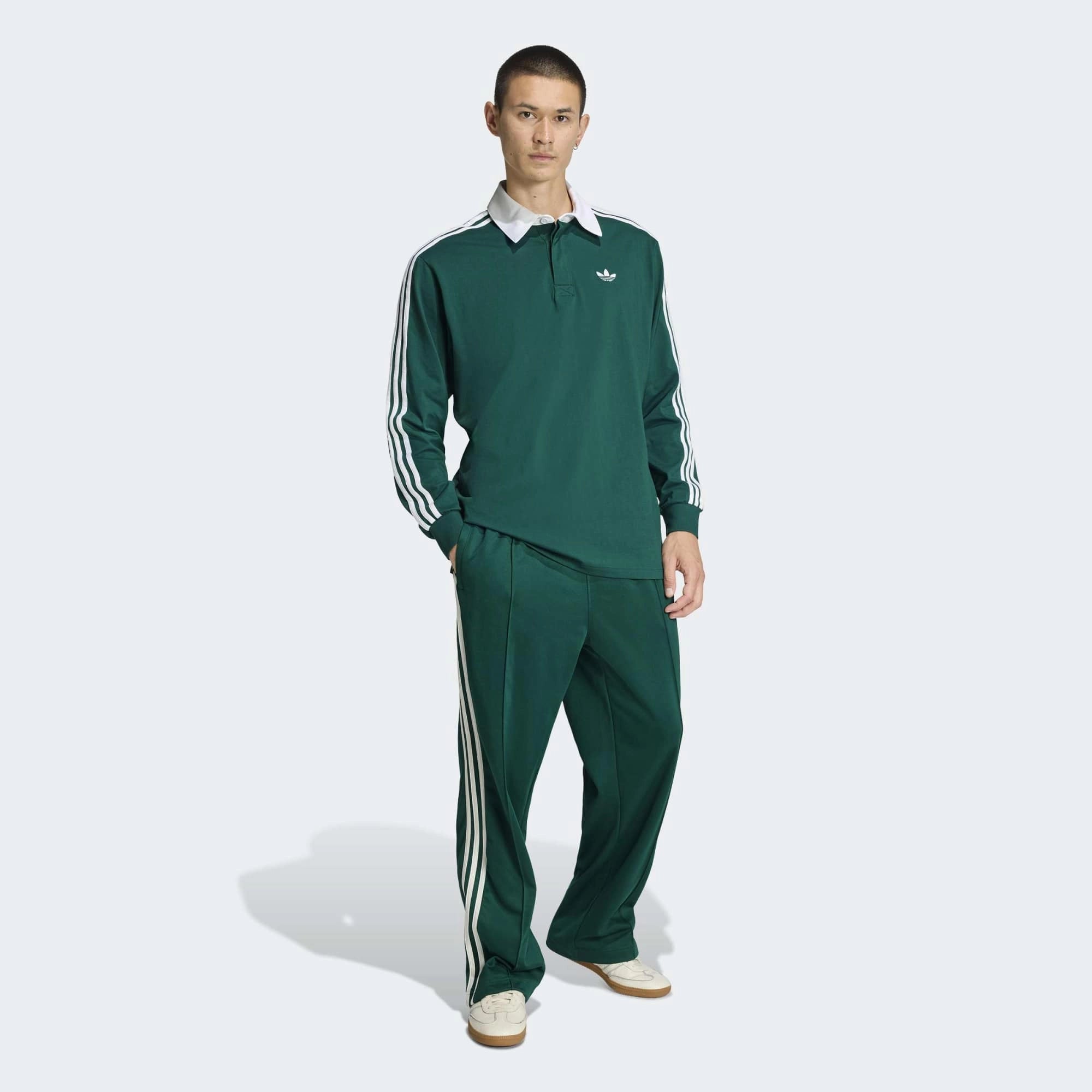 “Frontansicht Model Outfit der adidas Originals Baggy Track Pants in Collegiate Green mit weißen 3-Streifen, seitlichen Reißverschlusstaschen und weitem Beinabschluss bei Stickabush.“

