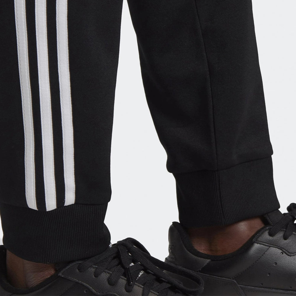 "Schwarze adidas Classics SST Trainingshose mit weißen 3-Streifen, Trefoil-Logo und schmal zulaufendem Bein bei Stickabush Berlin."