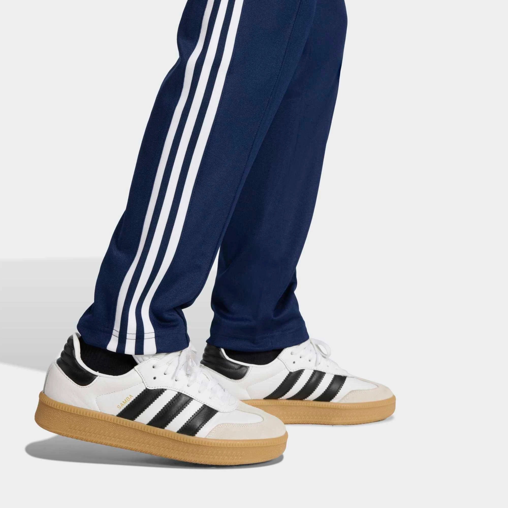 „Dunkelblaue Adidas Originals Beckenbauer Track Pant (Night Indigo) mit weißen 3-Streifen und klassischer Bügelfalte bei Stickabush Berlin.“
