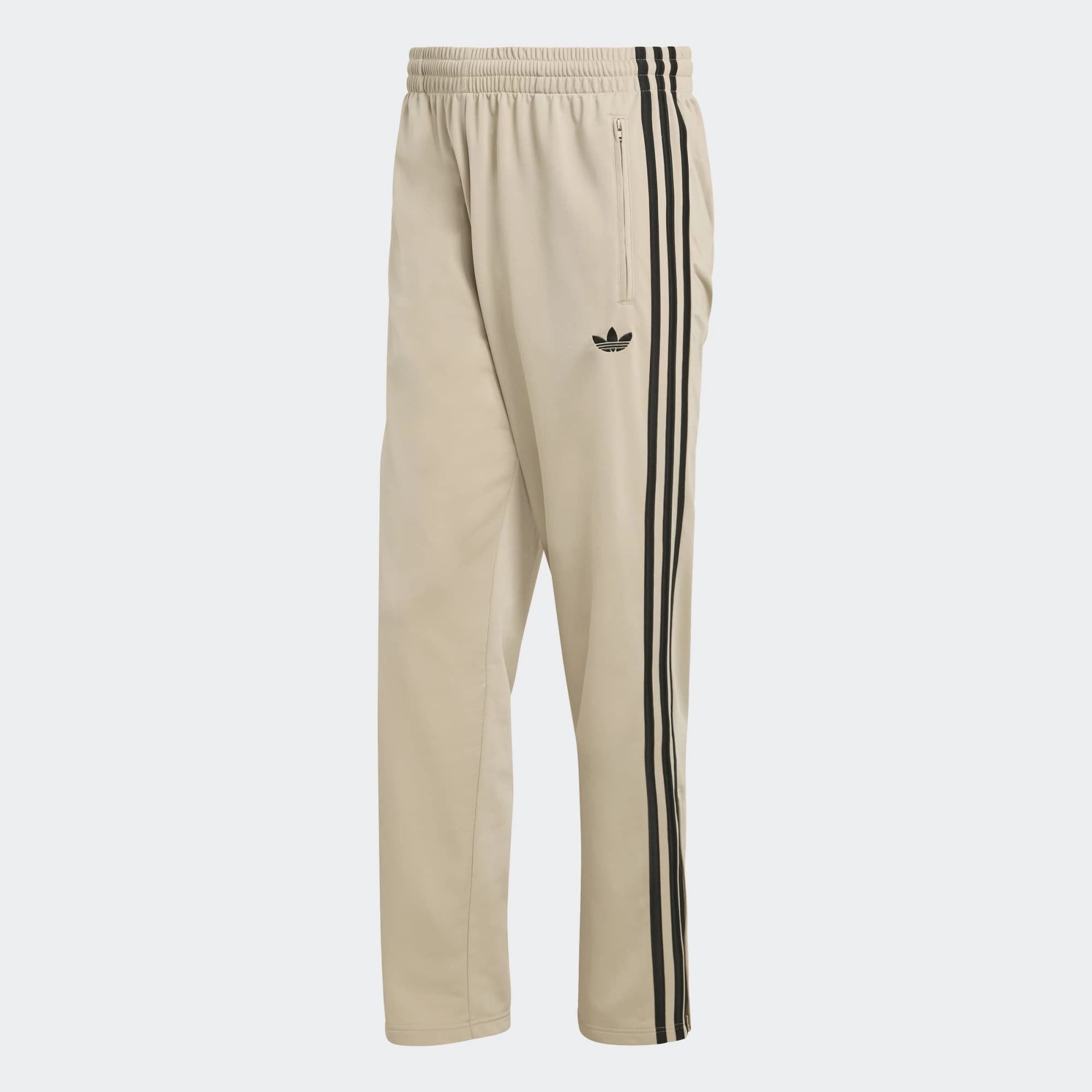 “Adidas Originals Firebird Track Pants in Stone Khaki mit schwarzen Streifen und gesticktem Trefoil-Logo bei Stickabush Berlin.“
