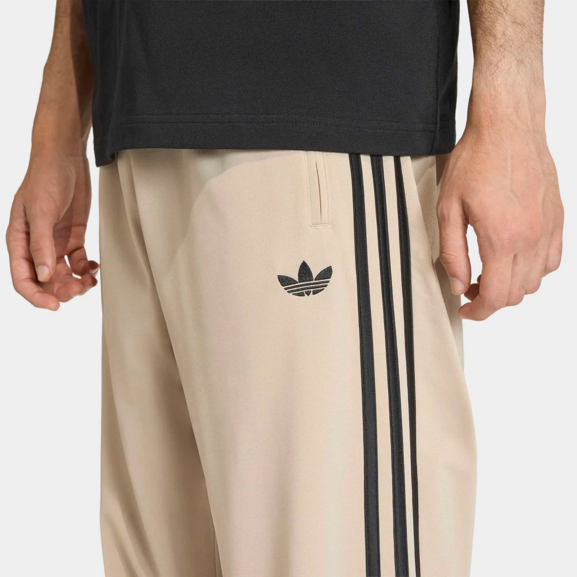 “Adidas Originals Firebird Track Pants in Stone Khaki mit schwarzen Streifen und gesticktem Trefoil-Logo bei Stickabush Berlin.“