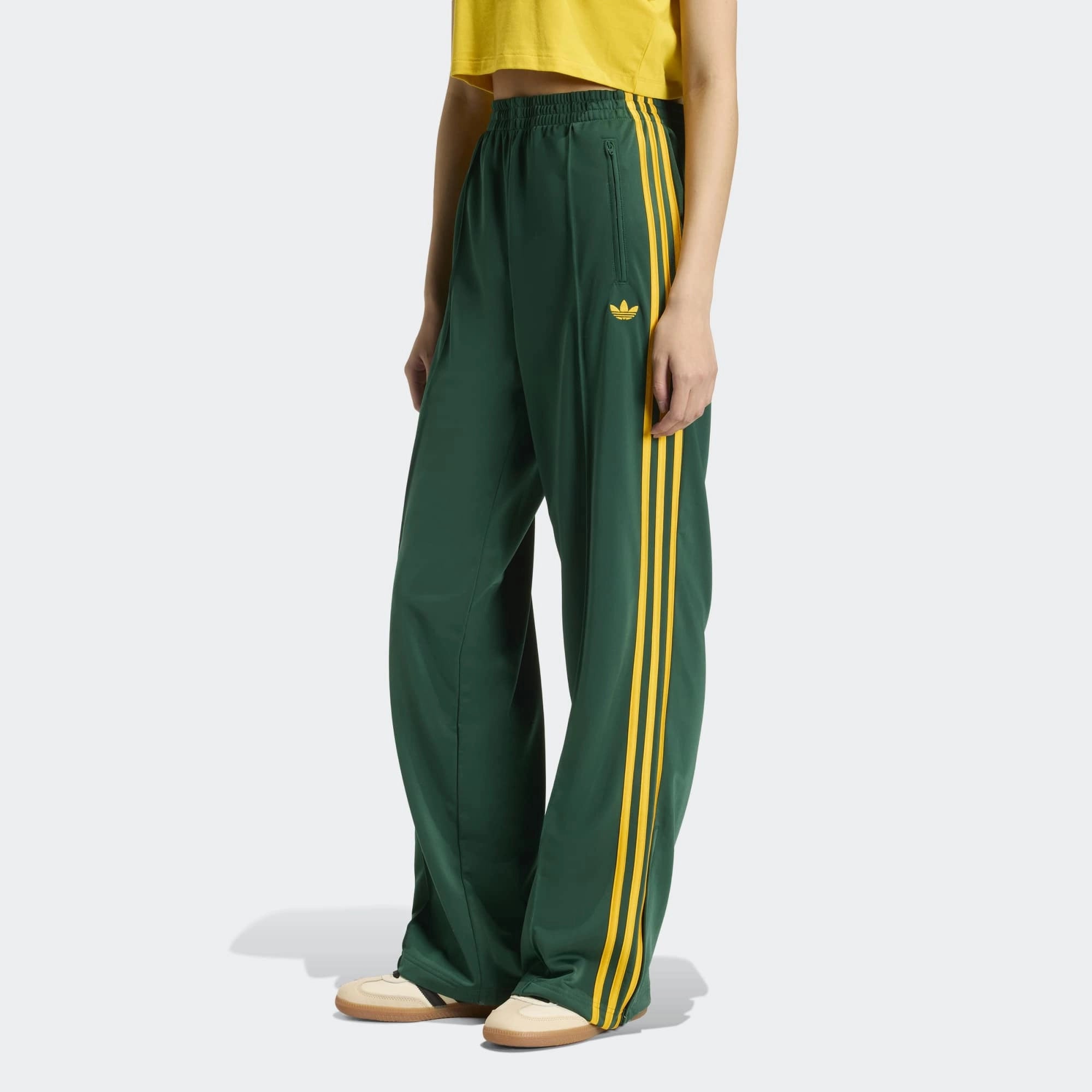 „Vorderansicht Model der Adidas Originals Firebird Loose Track Pants W in Collegiate Green mit Crew Yellow 3-Streifen – Weit geschnittene Damen-Trainingshose aus glänzendem Trikot bei Stickabush Berlin.“