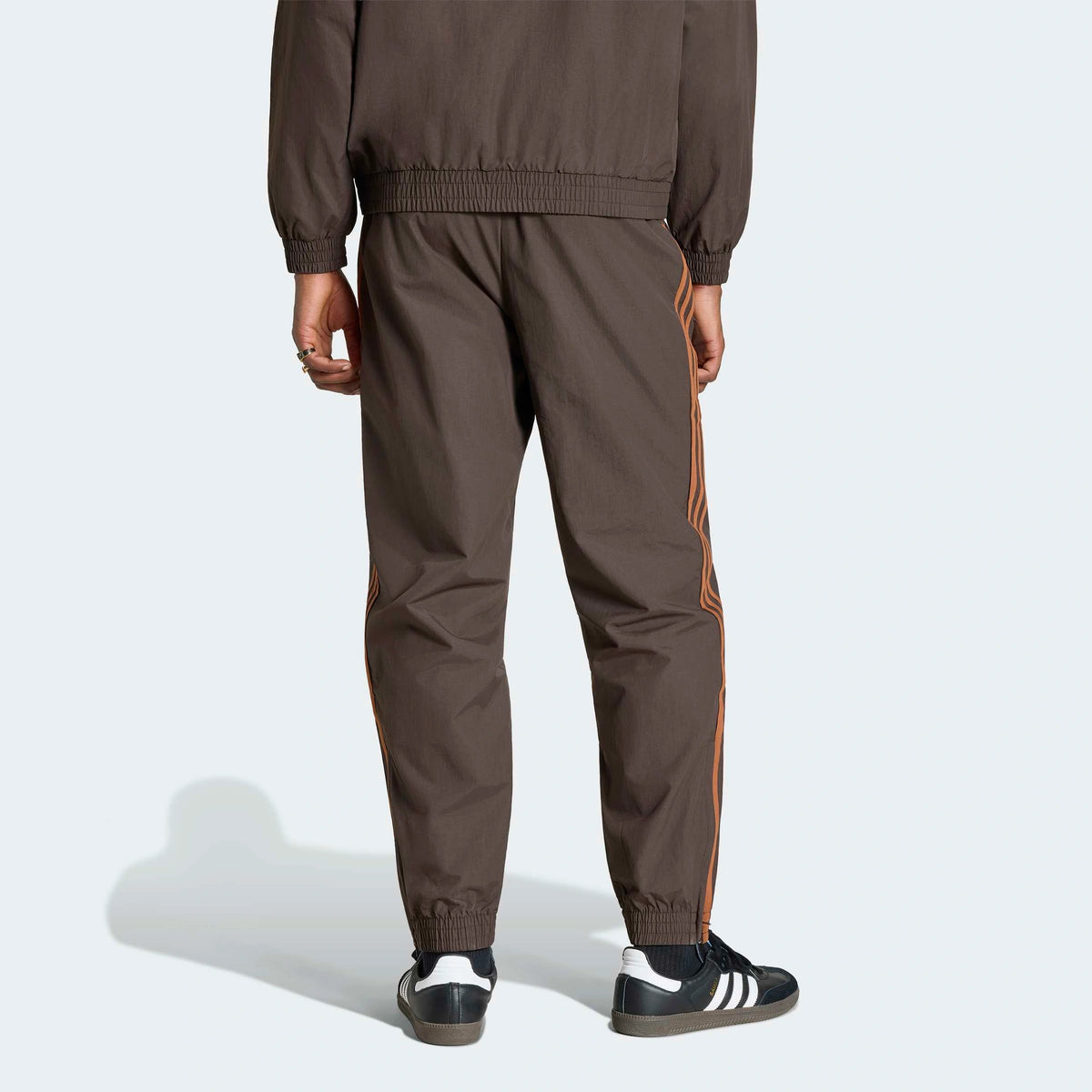 adidas Originals Firebird Woven Track Pants in Aurora Coffee – Rueckansicht am Model der braunen Trainingshose aus Webmaterial mit den ikonischen 3-Stripes.