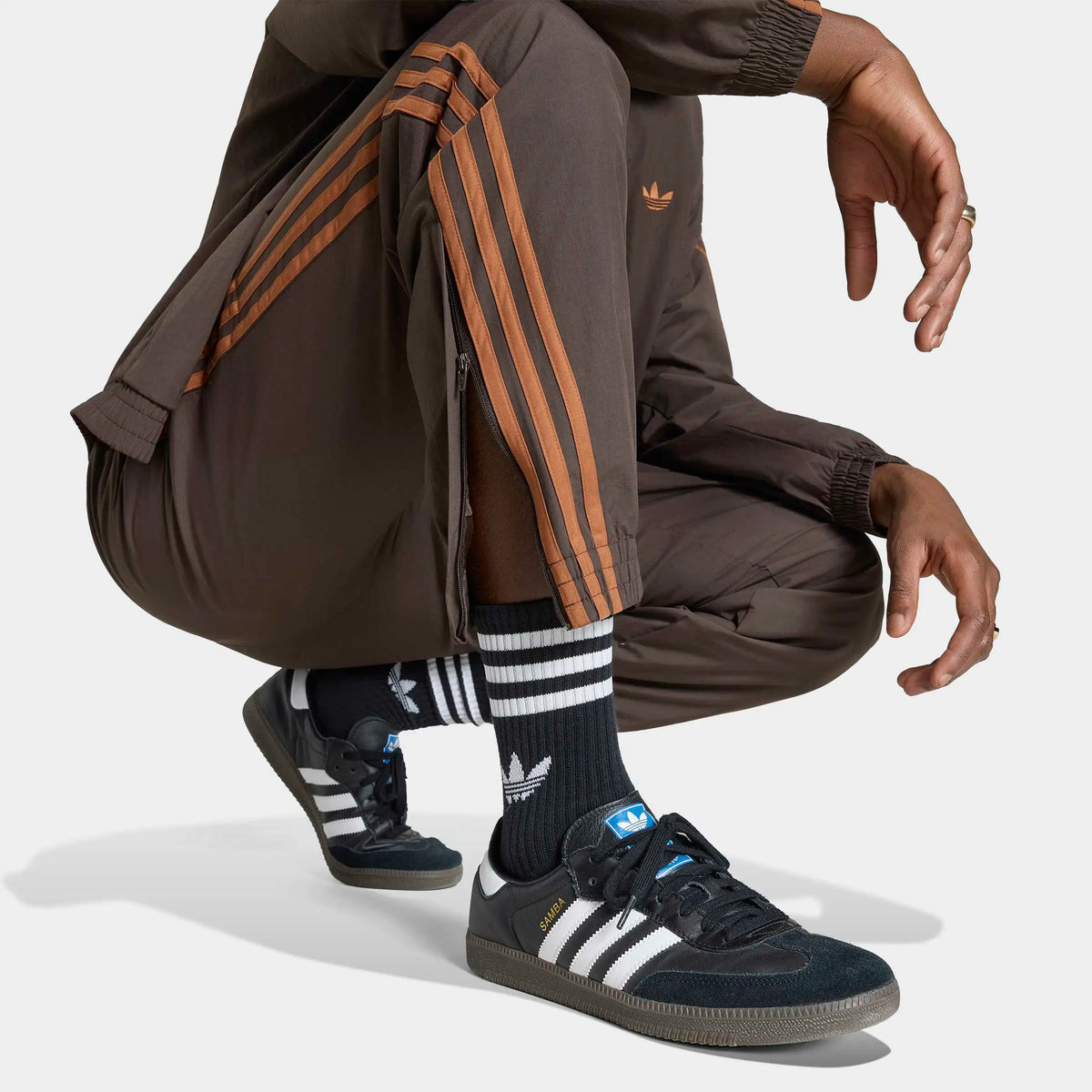 adidas Originals Firebird Woven Track Pants in Aurora Coffee – Vorderansicht Details am Model der braunen Trainingshose aus Webmaterial mit den ikonischen 3-Stripes.