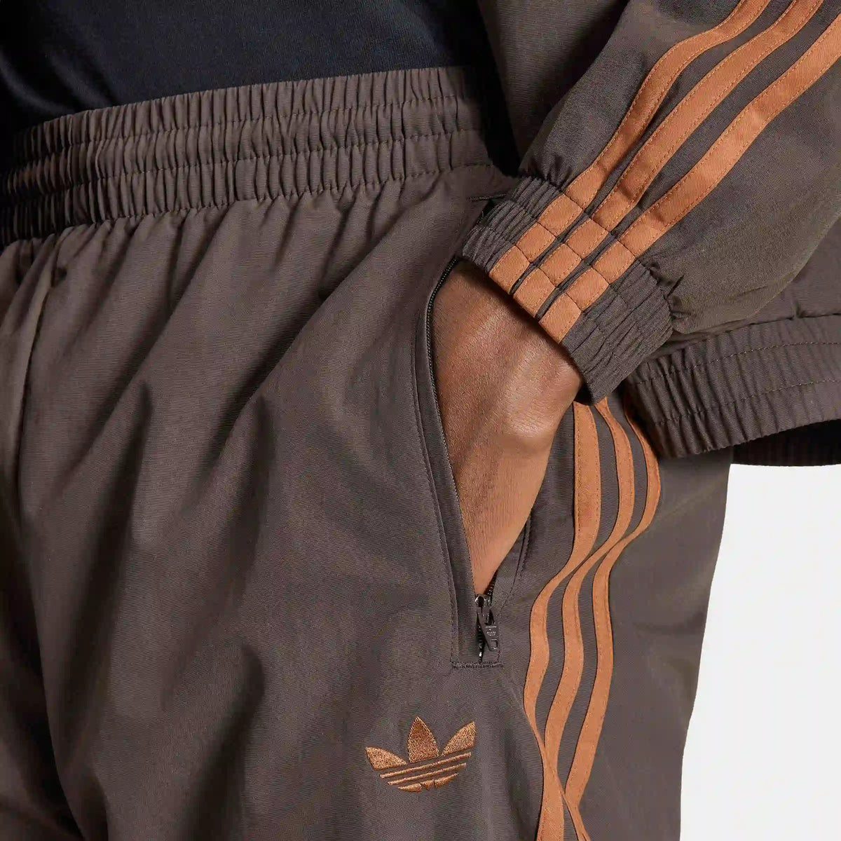 adidas Originals Firebird Woven Track Pants in Aurora Coffee – Vorderansicht Details am Model der braunen Trainingshose aus Webmaterial mit den ikonischen 3-Stripes.