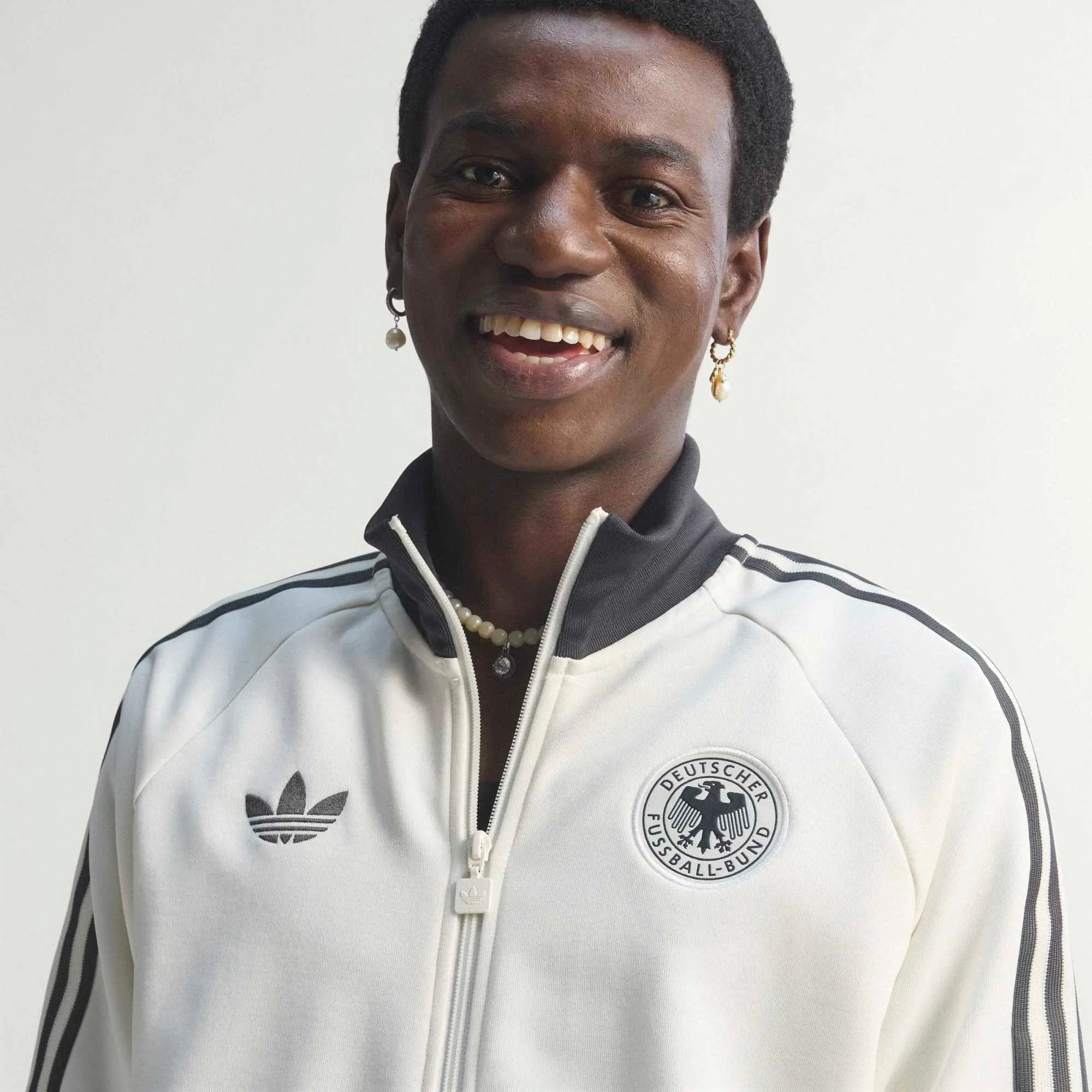 “Cremeweiße adidas Originals DFB Deutschland OG Trainingsjacke mit schwarzen Streifen und gesticktem DFB-Logo bei Stickabush.“