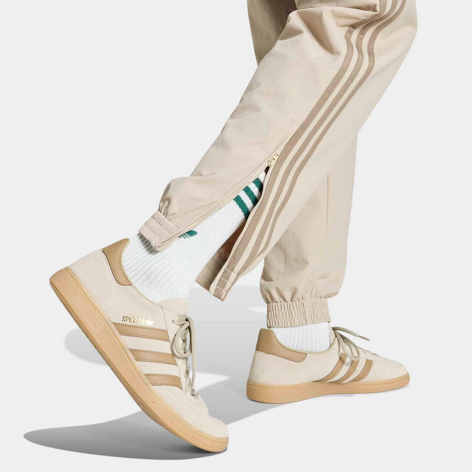 „Beigefarbene adidas Originals Firebird Woven Track Pants (KS7503) aus gewebtem Material mit weißen Streifen – leichte Damen-Trainingshose im Retro-Stil erhältlich bei Stickabush Berlin.“