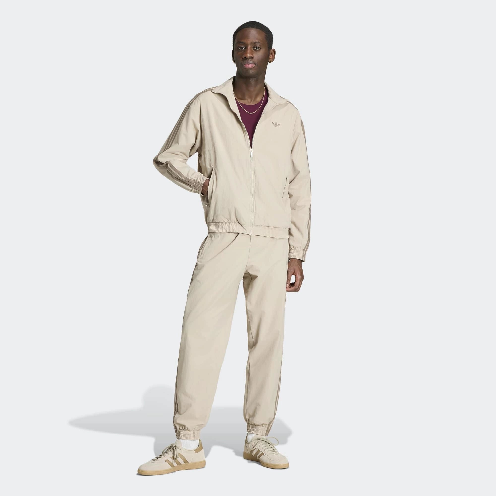„Beigefarbene adidas Originals Firebird Woven Track Pants (KS7503) aus gewebtem Material mit weißen Streifen – leichte Damen-Trainingshose im Retro-Stil erhältlich bei Stickabush Berlin.“