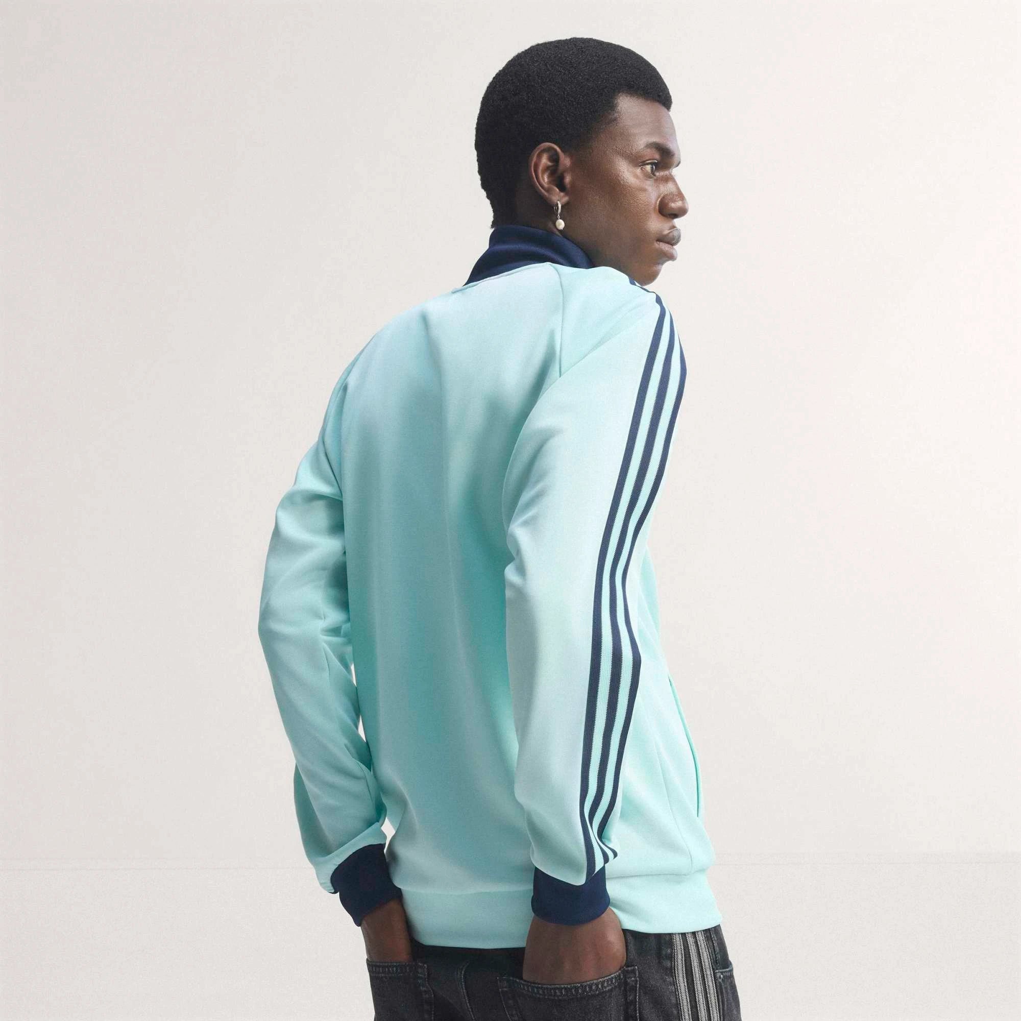“Die türkise adidas Originals Deutschland OG Trainingsjacke (Semi Flash Aqua) mit klassischen weißen 3-Streifen und Retro-Details bei Stickabush“.