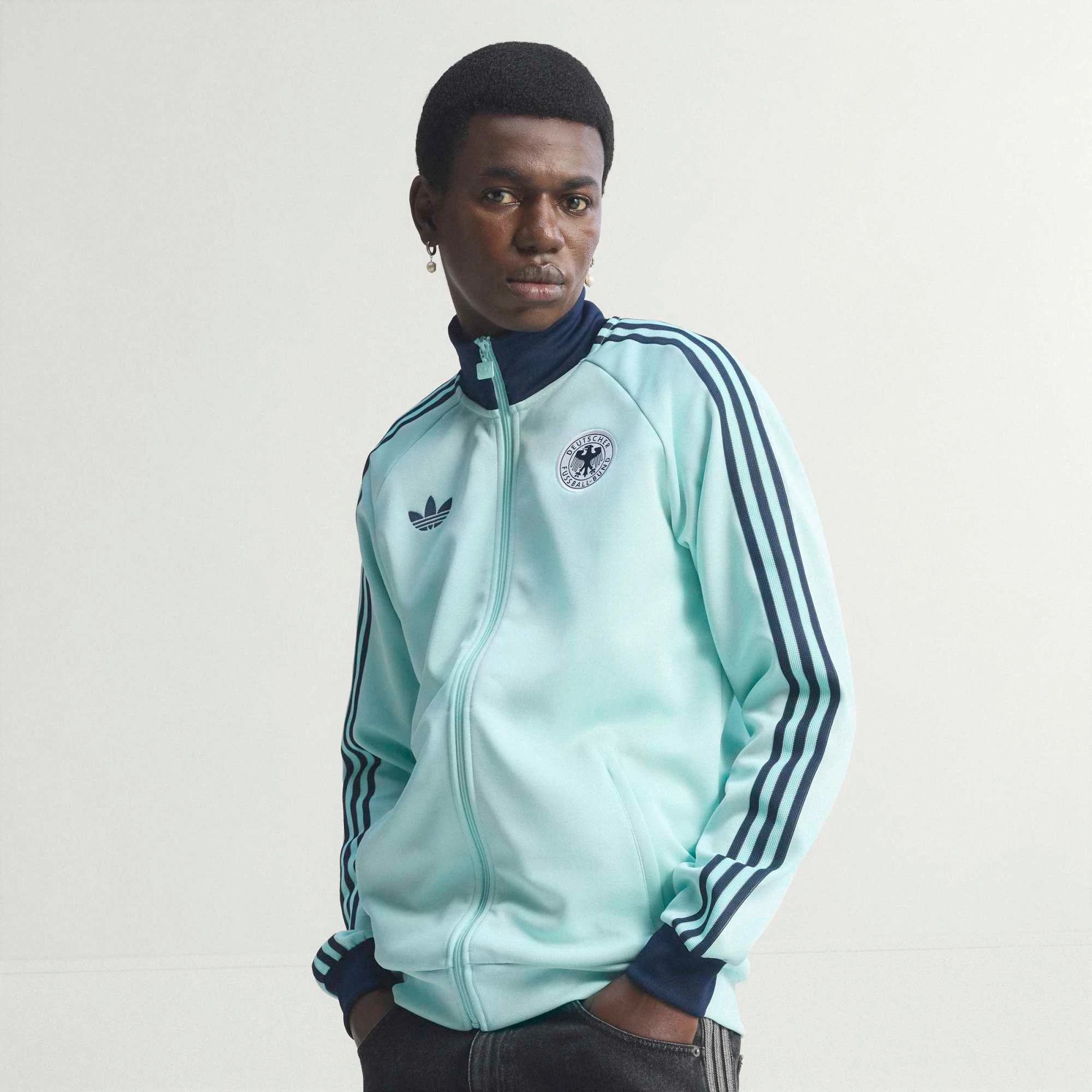 “Die türkise adidas Originals Deutschland OG Trainingsjacke (Semi Flash Aqua) mit klassischen weißen 3-Streifen und Retro-Details bei Stickabush“.