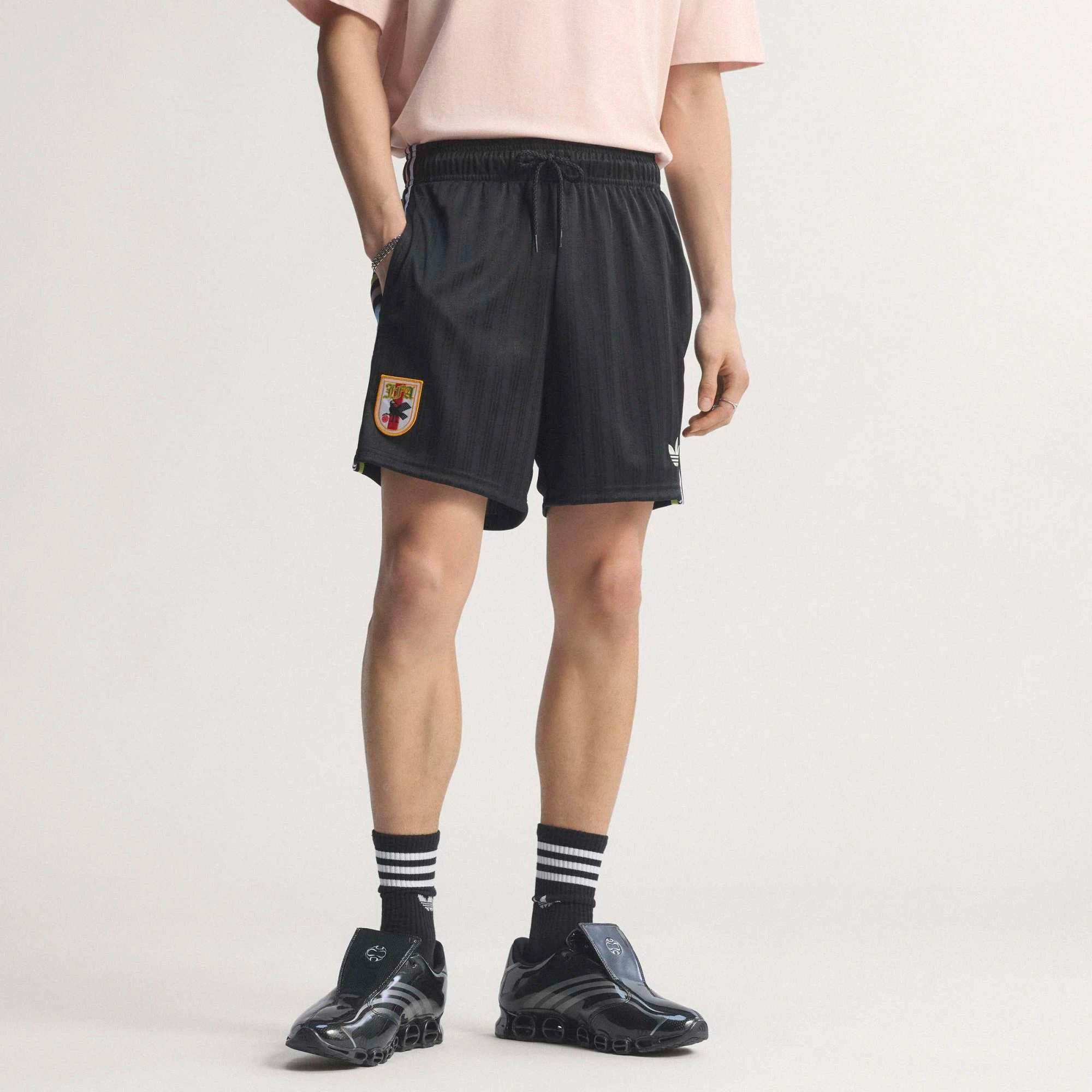 “Schwarze adidas Originals Japan OG Shorts mit weißen Streifen und dem gestickten JFA Japan Verbandswappen bei Stickabush.“