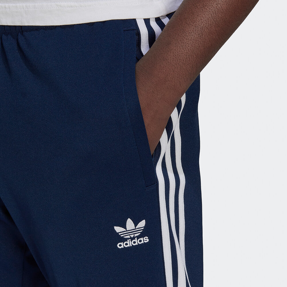 "Dunkelblaue adidas Classics SST Track Pant (Night Indigo) mit weißen 3-Streifen, Trefoil-Stickerei und Reißverschlusstaschen bei Stickabush Berlin."