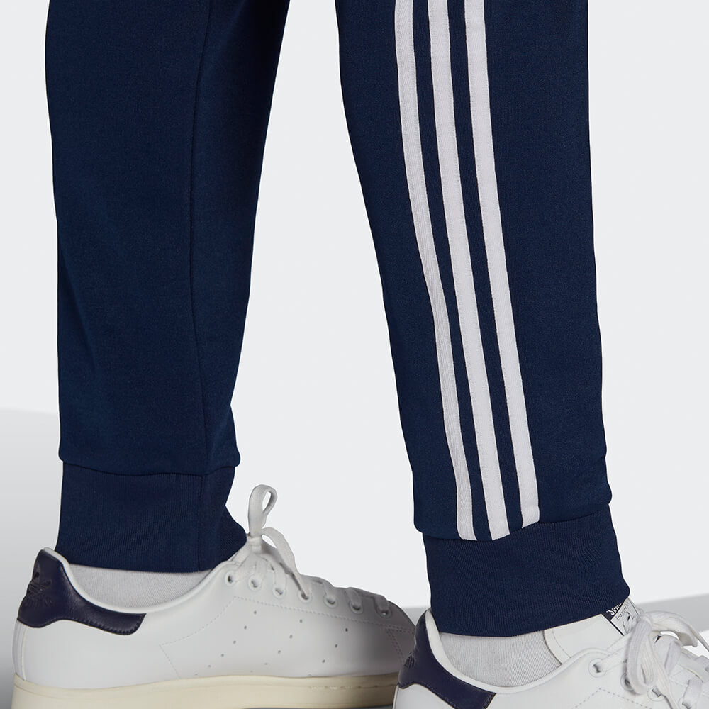 "Dunkelblaue adidas Originals SST Track Pant (Night Indigo) mit weißen 3-Streifen, Trefoil-Stickerei und Reißverschlusstaschen bei Stickabush Berlin."